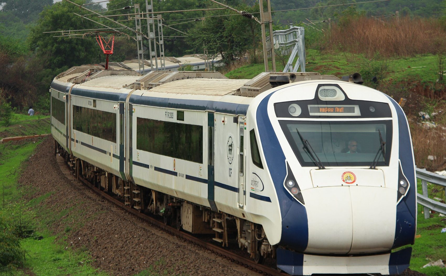 Vande Bharat Express rounding a curve on a green hillside