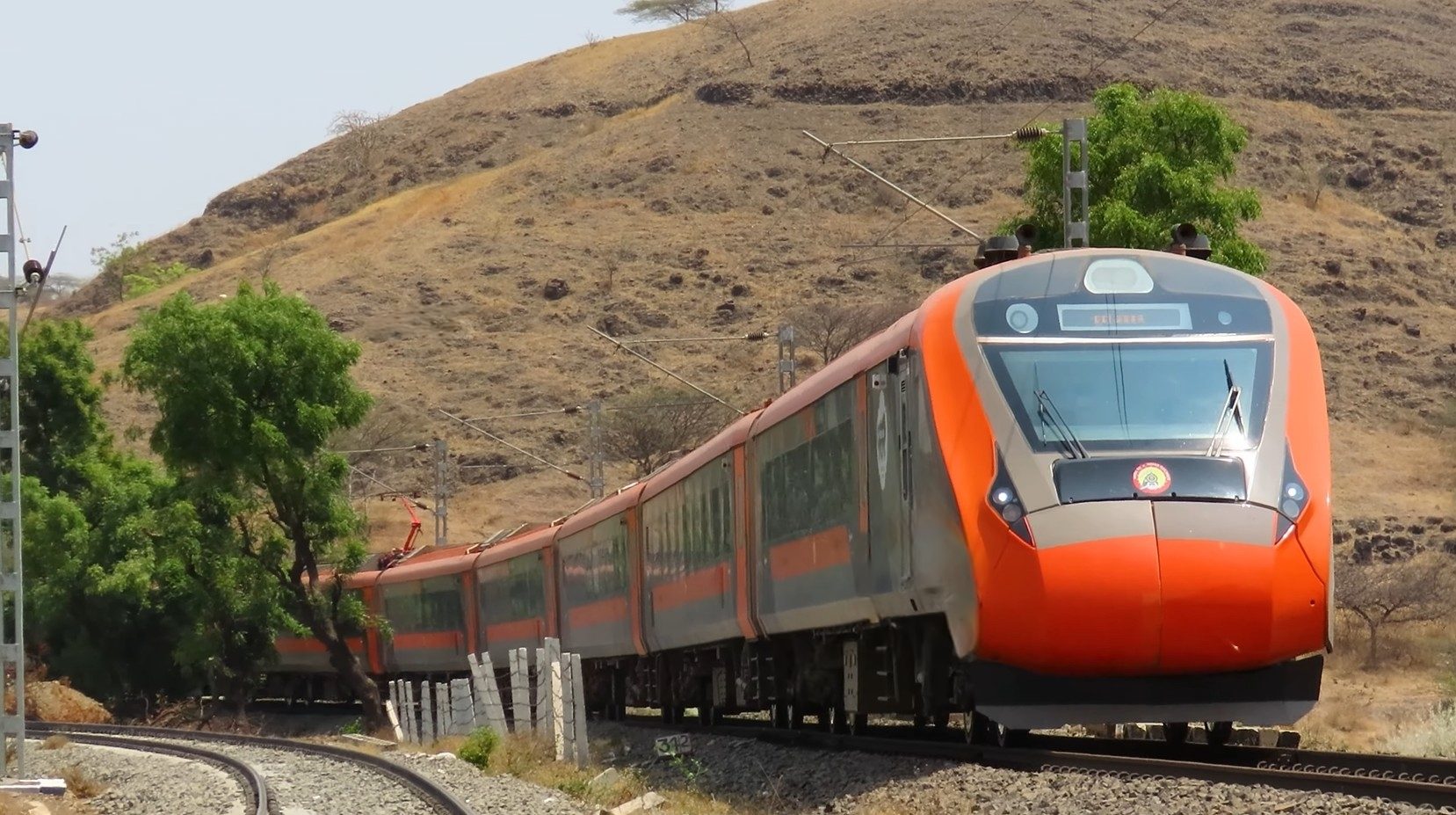 Orange Vande Bharat Express on a hill curve